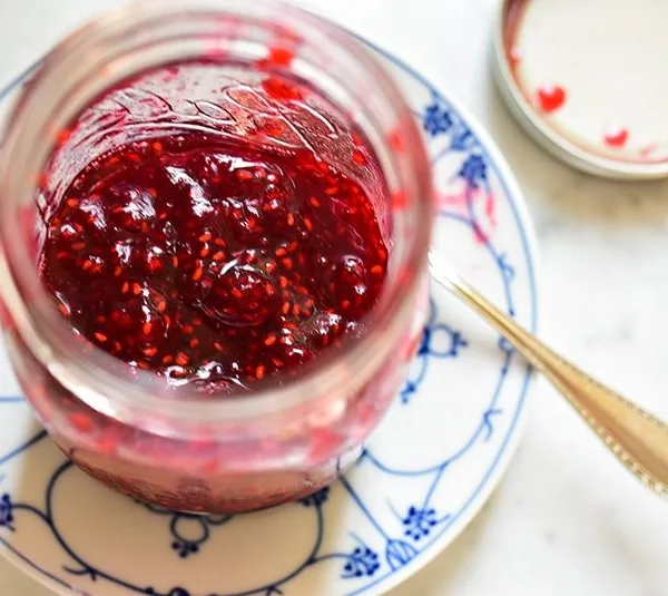 Open top of jar of simple raspberry jam in a Ball jar on a blue and white plate with spoon