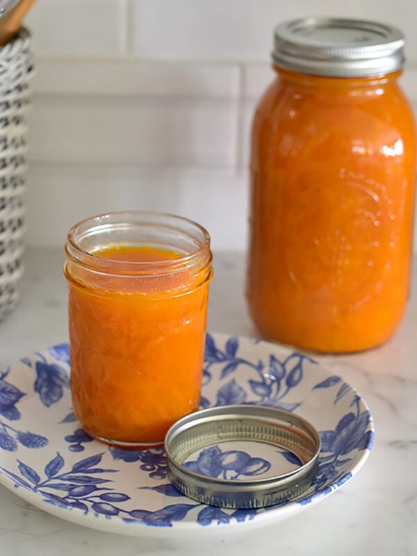 Apricot jam in two jars on a marble counter with blue and white plate