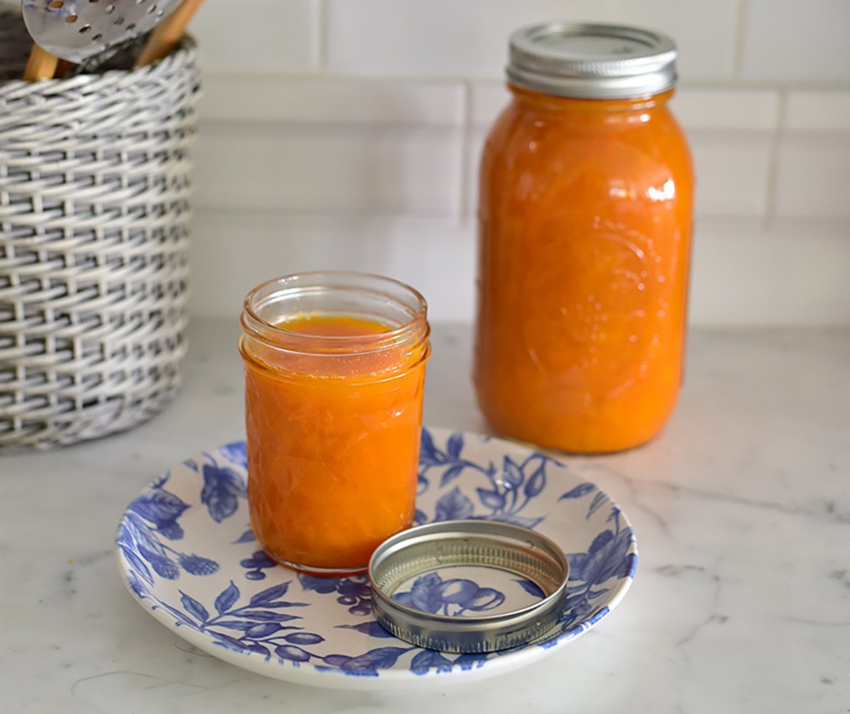 Apricot jam in two jars on a marble counter with blue and white plate