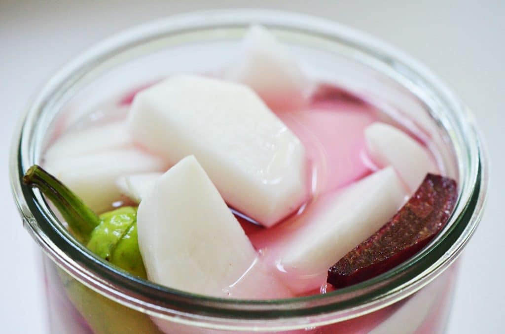 top view of an open jar filled with cut turnips, jalepeño and beets for pickles