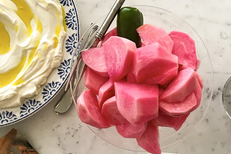 Pink turnip pickles in a dish next to a bowl of white labneh with olive oil