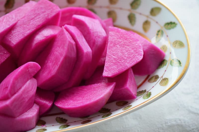 Pink turnip pickle slices in a green and white serving dish