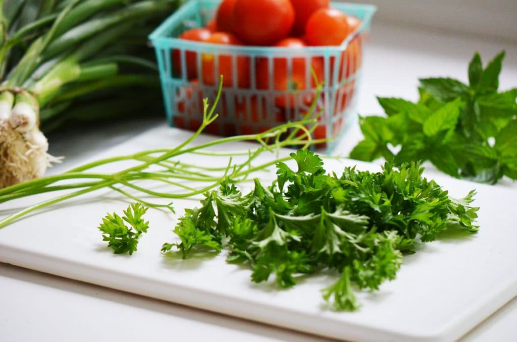 Parsley leaves picked from the stems on a cutting board with a box of tomatoes on the side