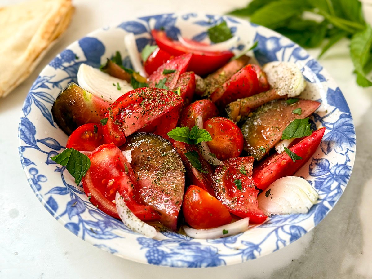 Tomato Salad in a blue and white bowl with mint on the side
