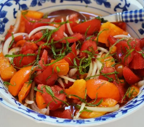 Red and yellow tomatoes with onion and mint in a blue salad bowl