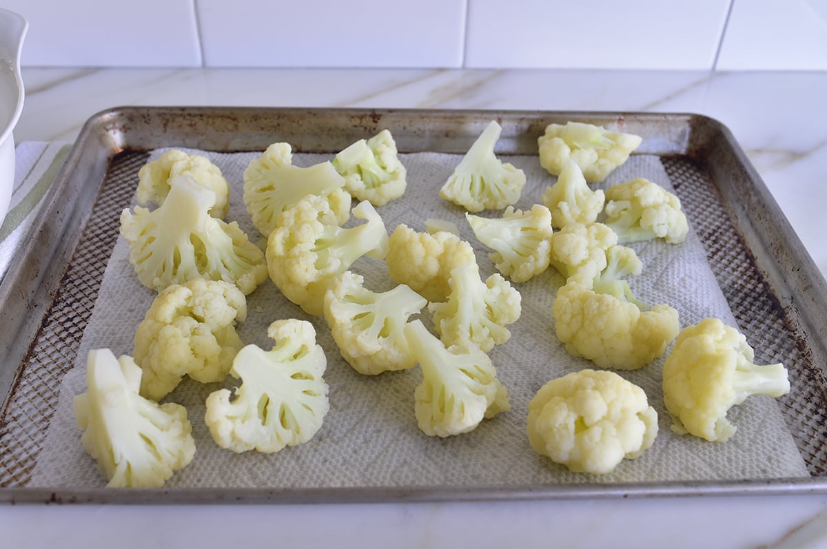 Par-cooked cauliflower florets on a paper towel lined baking sheet