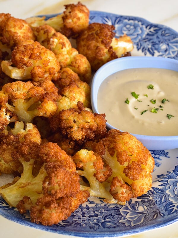 Fried cauliflower on a blue and white platter with tahini sauce on the side