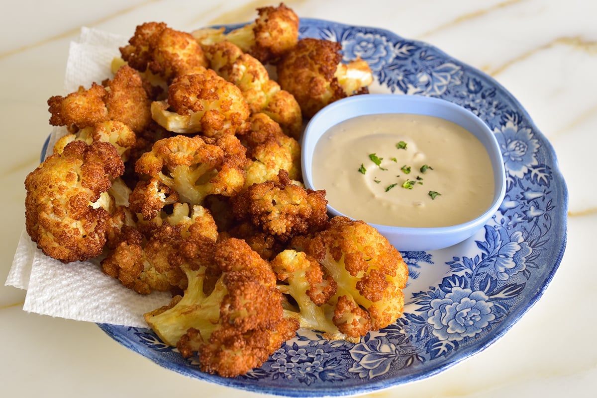 Fried cauliflower on a blue and white platter with tahini sauce on the side
