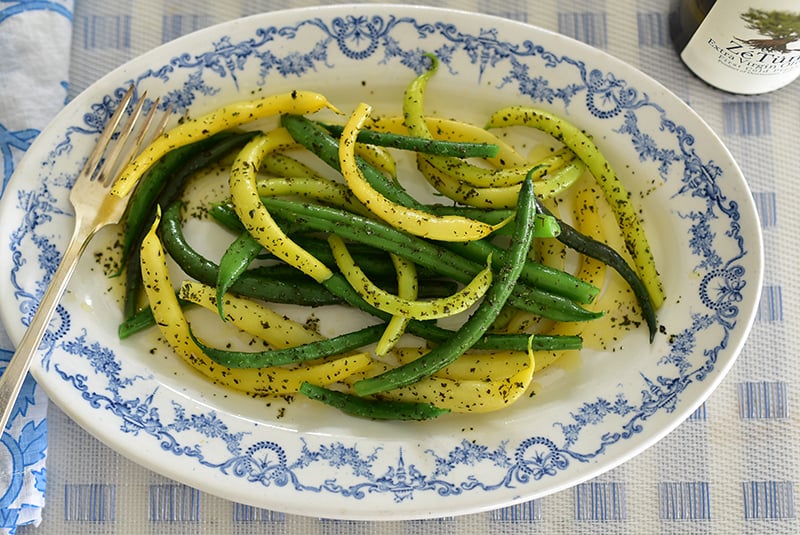 green and white beans on a blue and white plate with olive oil and flecks of mint