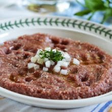 Raw beef kibbeh on a plate with onions and herbs on top