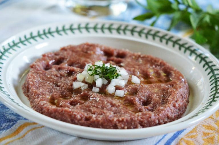 Raw beef kibbeh on a plate with onions and herbs on top