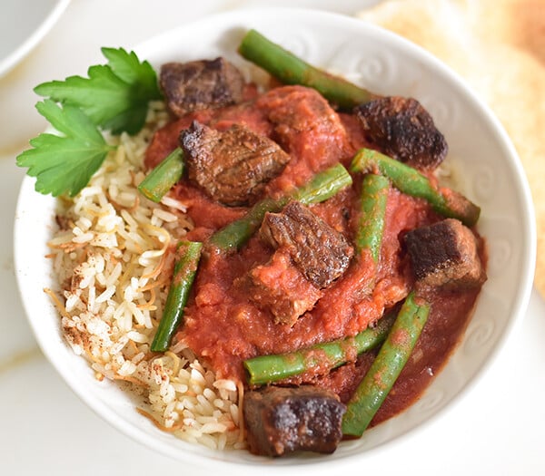 Green bean stew with meat on a bed of rice in a white bowl