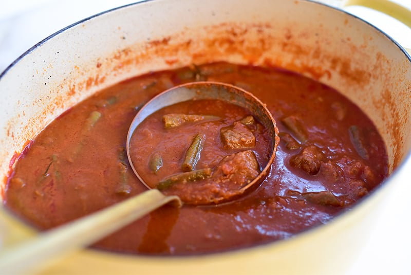 Tomato stew with meat and green beans with a copper ladle in the pot