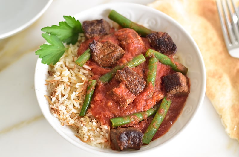 Green bean stew with meat on a bed of rice in a white bowl