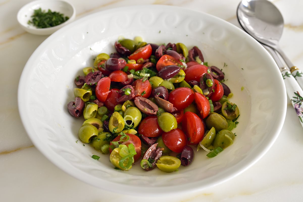 A white bowl with olive salad mixed together and a spoon alongside