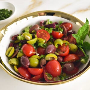 olive salad with tomatoes and mint in a gold-rimmed bowl