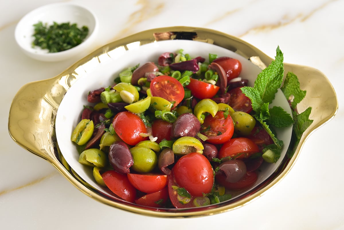 olive salad with tomatoes and mint in a gold-rimmed bowl