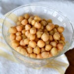 Chickpeas in a glass bowl with a yellow and white cloth underneath it