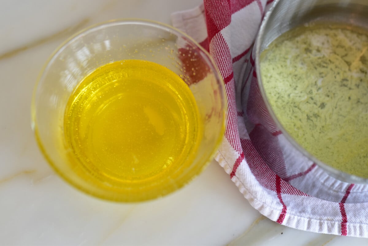 golden clarified butter in a glass bowl next to a pan and red and white towel