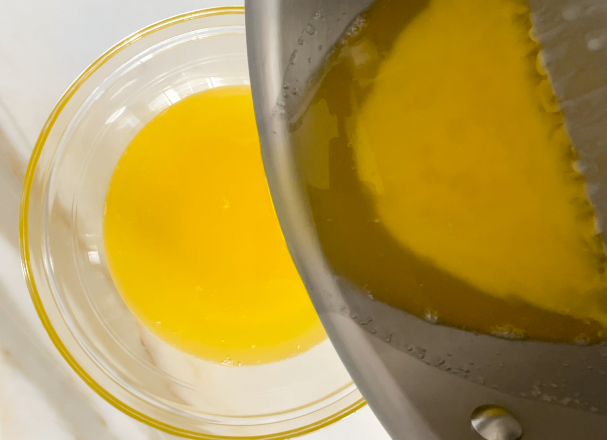 Clarified butter in a glass bowl with a pan of butter being poured into it