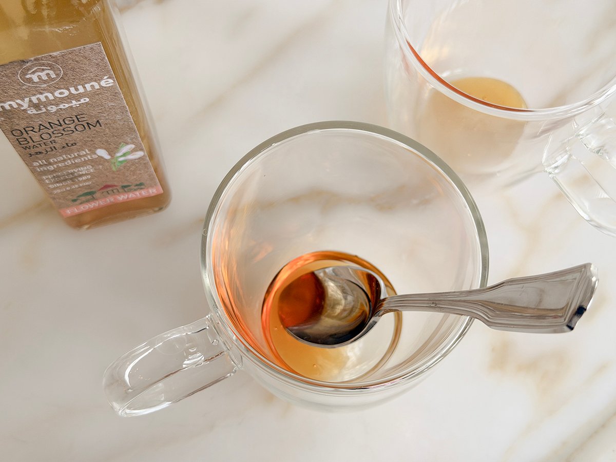 A clear mug with a silver spoon it with some honey