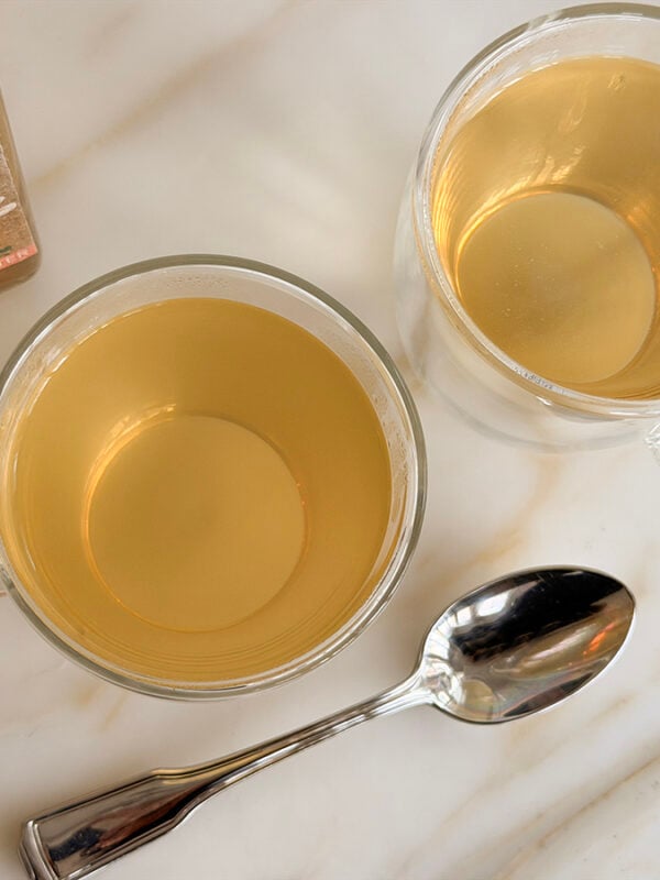 Two clear mugs with a spoon and orange blossom water on the side