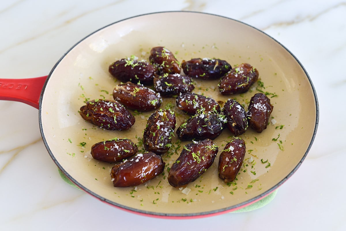 Dates topped with lime zest and sea salt in an enameled saute pan