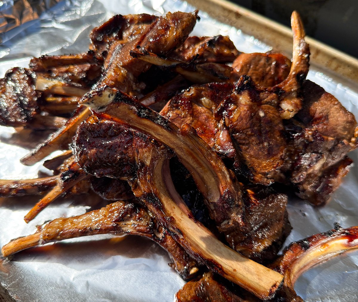 Lamb chops on foil lined baking sheet next to the grill