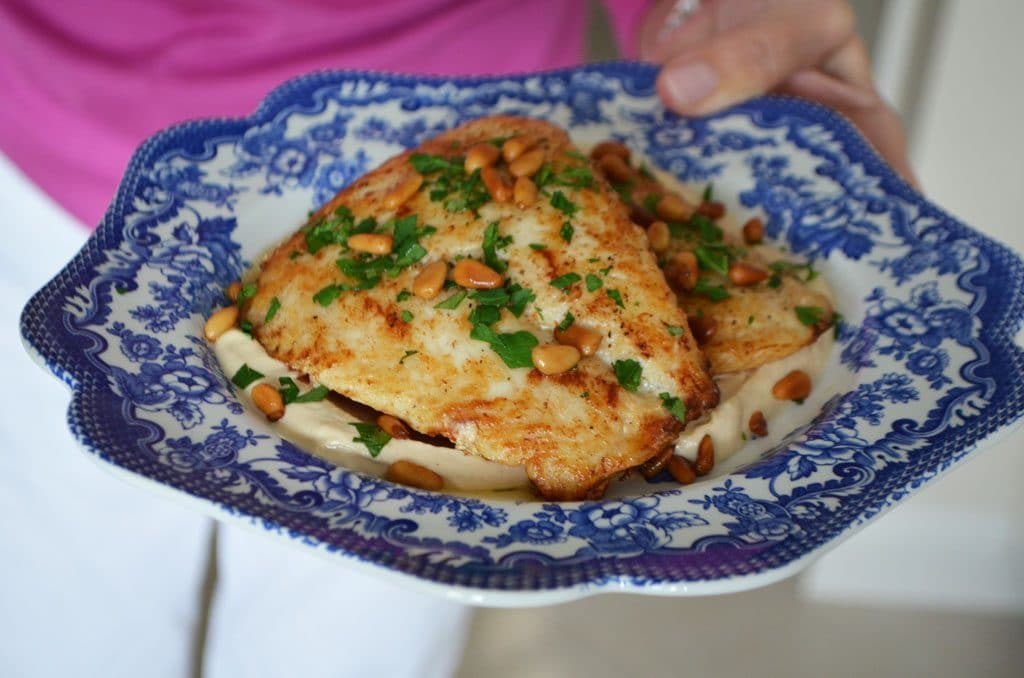 Golden fish filets on a blue plate sprinkled with pine nuts and parsley