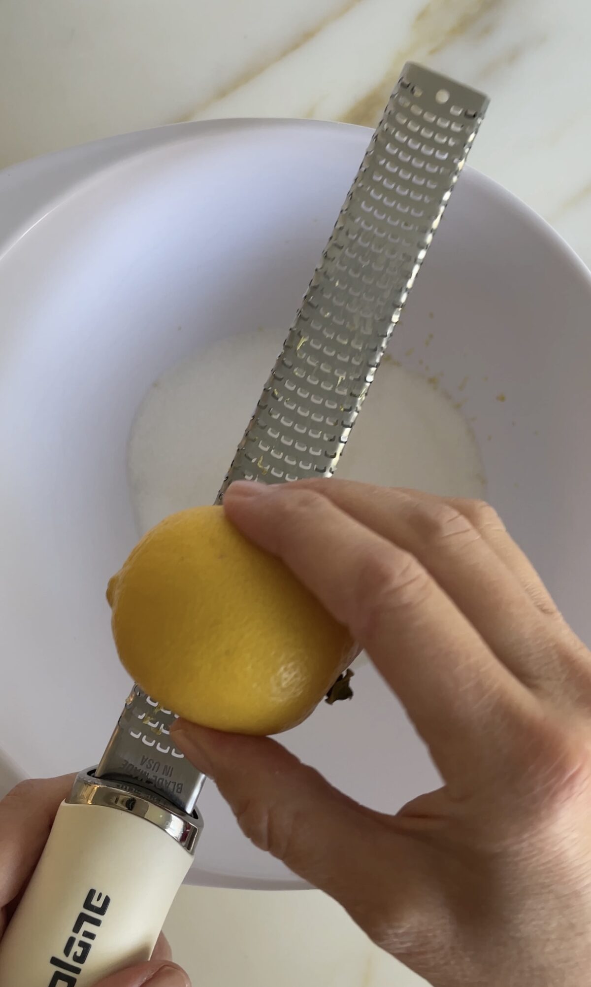 Lemon and a microplane zester with a hand over a white bowl