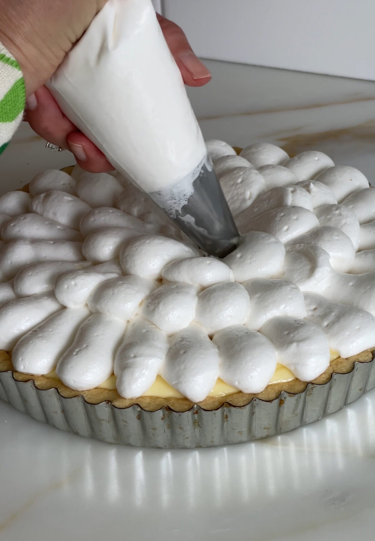 A piping bag with white meringue piped in a flower design on a tart
