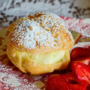 Cream puff with powdered sugar on top and strawberries on the side