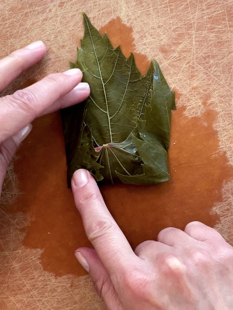 Two hands fold a grape leaf for grape leaf rolls