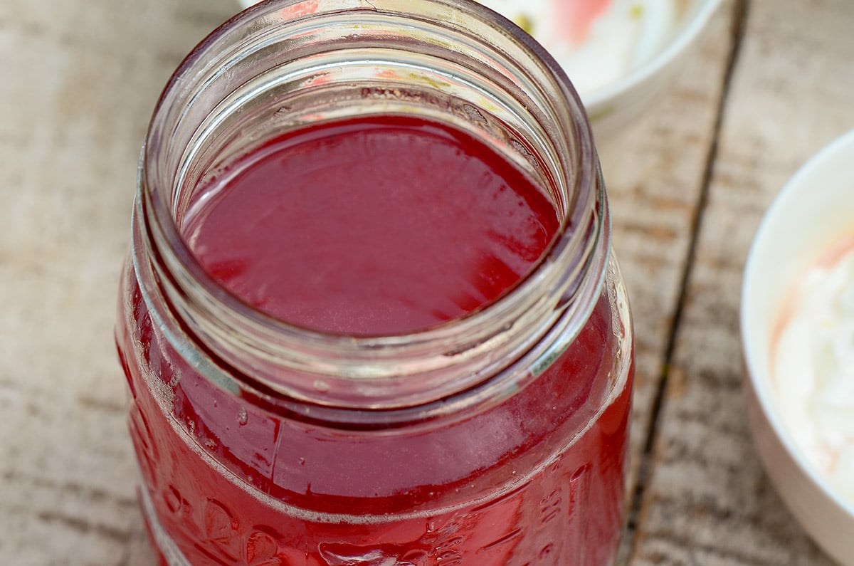 A jar of pink rhubarb syrup on a wood surface
