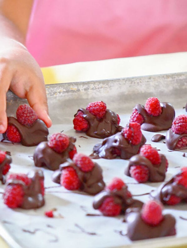 Chocolate covered raspberries with a child's hand and a pink shirt in the background