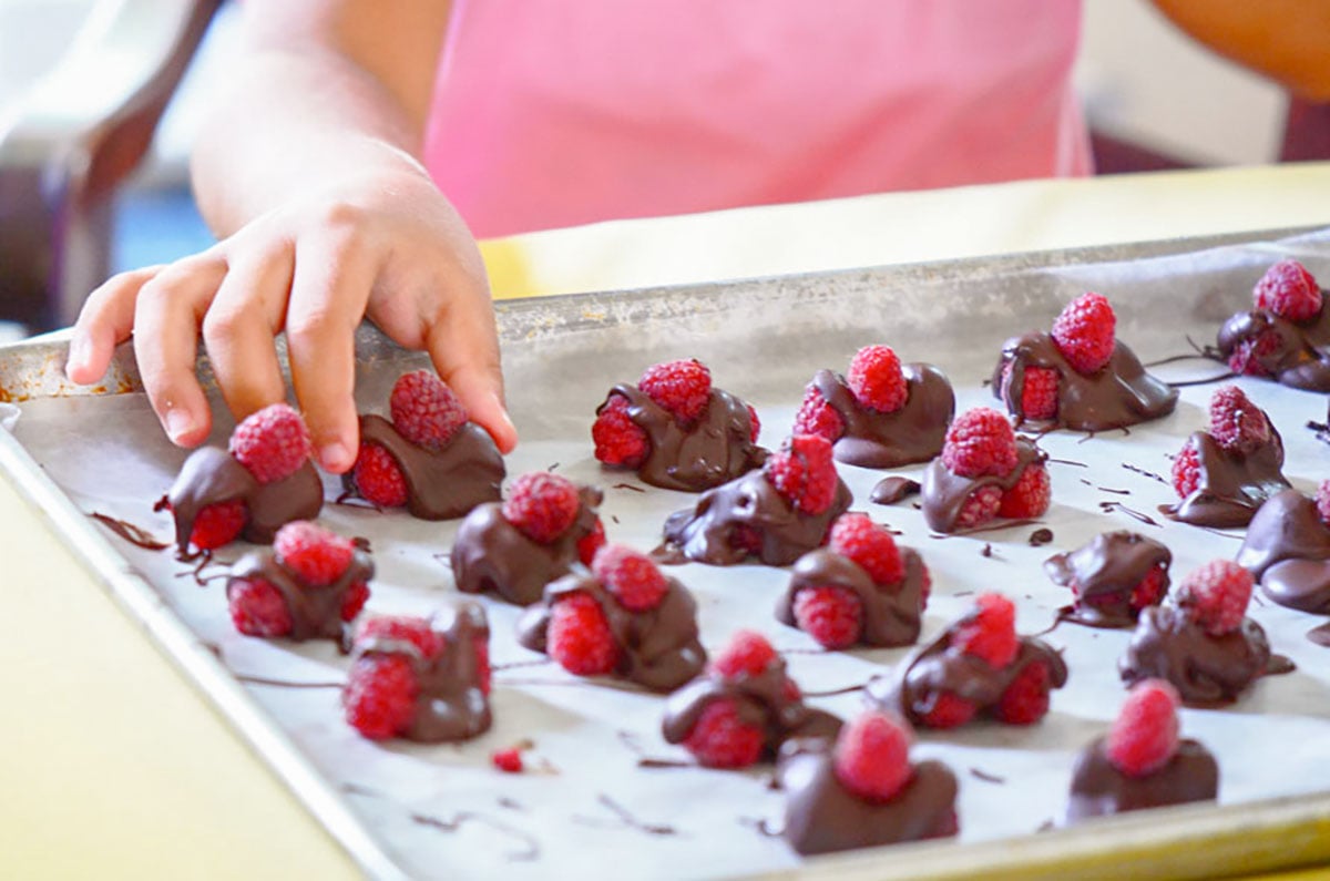 Chocolate covered raspberries with a child's hand and a pink shirt in the background