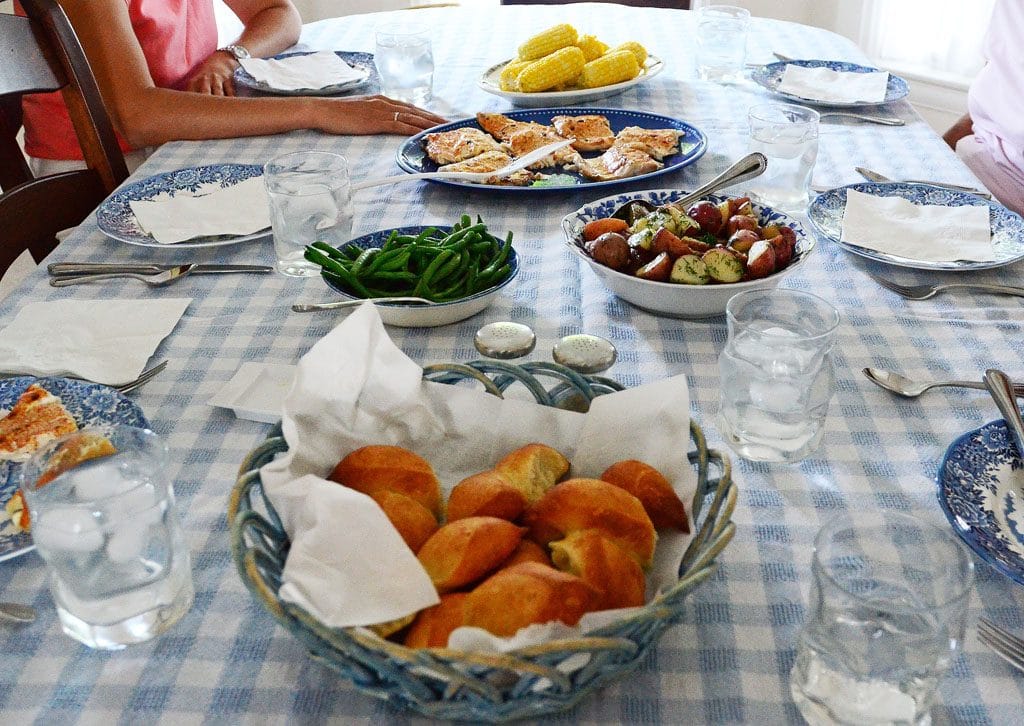 A table spread with blue and white tablecloth, whitefish, dinner rolls, green beans