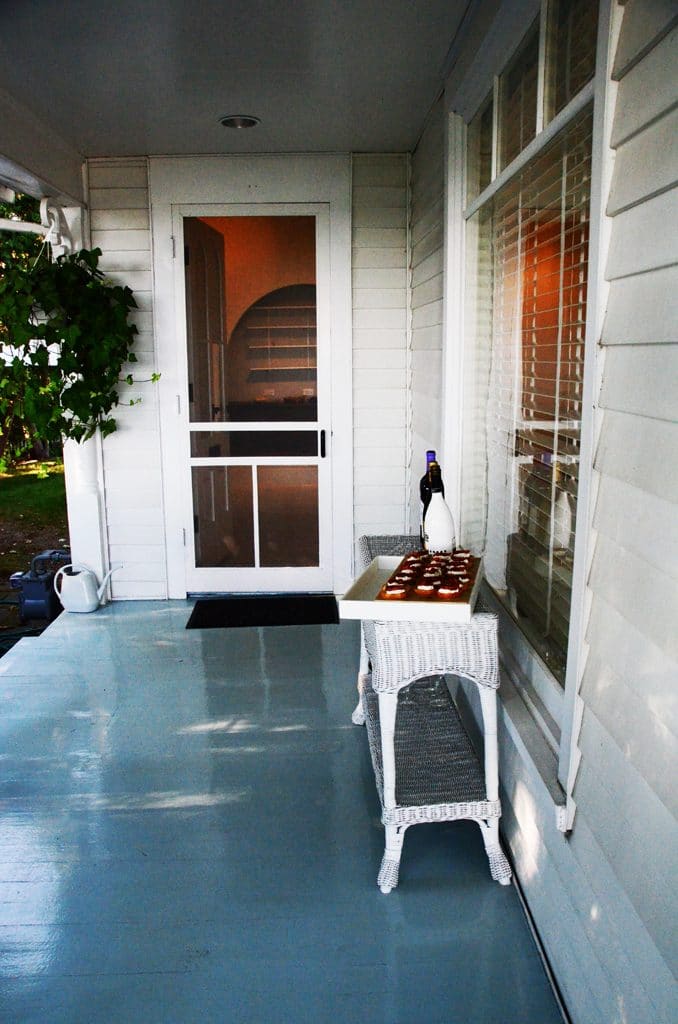 Front door to the house on the Bluff with gray painted porch floor and wicker furniture, Maureen Abood