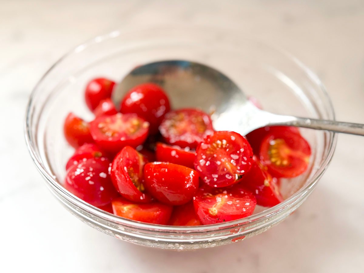 sliced cherry tomatoes in a bowl with salt and a spoon
