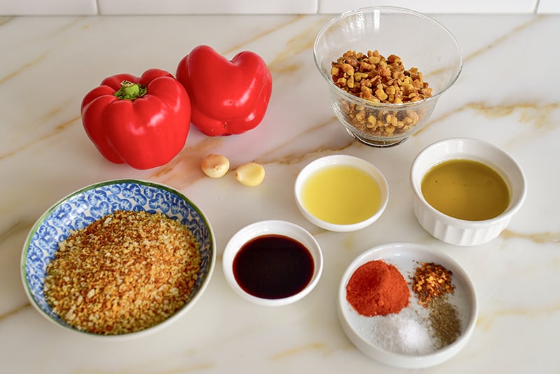 Ingredients for muhammara on the counter, red pepper and walnuts, olive oil, lemon juice, bread crumbs, spices