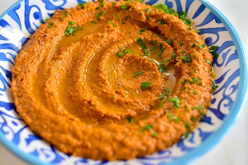 Red pepper dip on a blue and white dish topped with evoo and parsley