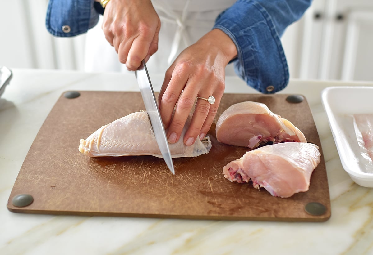 Hands cutting chicken breasts in half on a cutting board