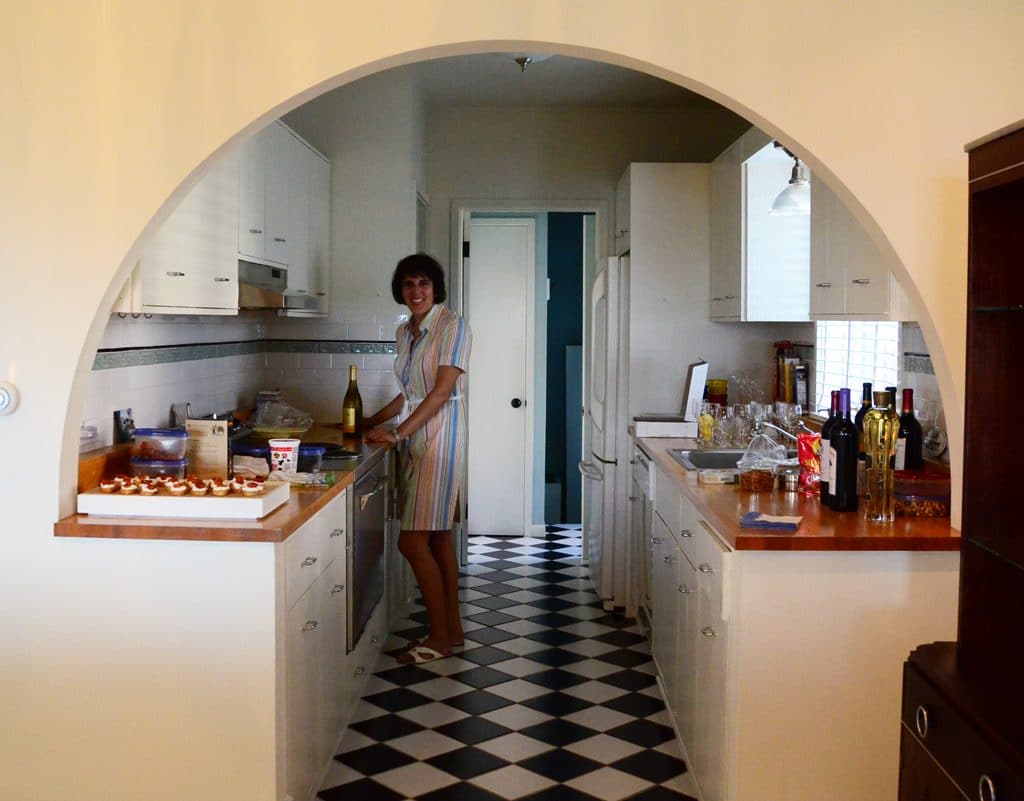 Peggy in the kitchen under a curved doorway with checkerboard floor, Maureen Abood