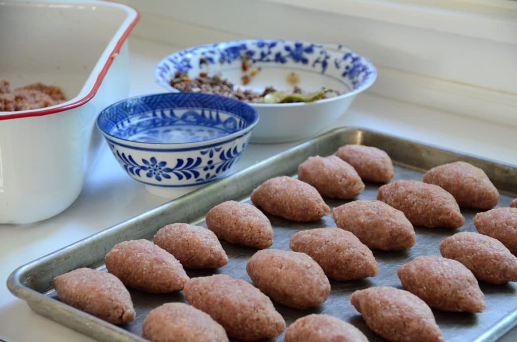 Shaped kibbeh footballs on a sheet pan with ingredients in bowls.