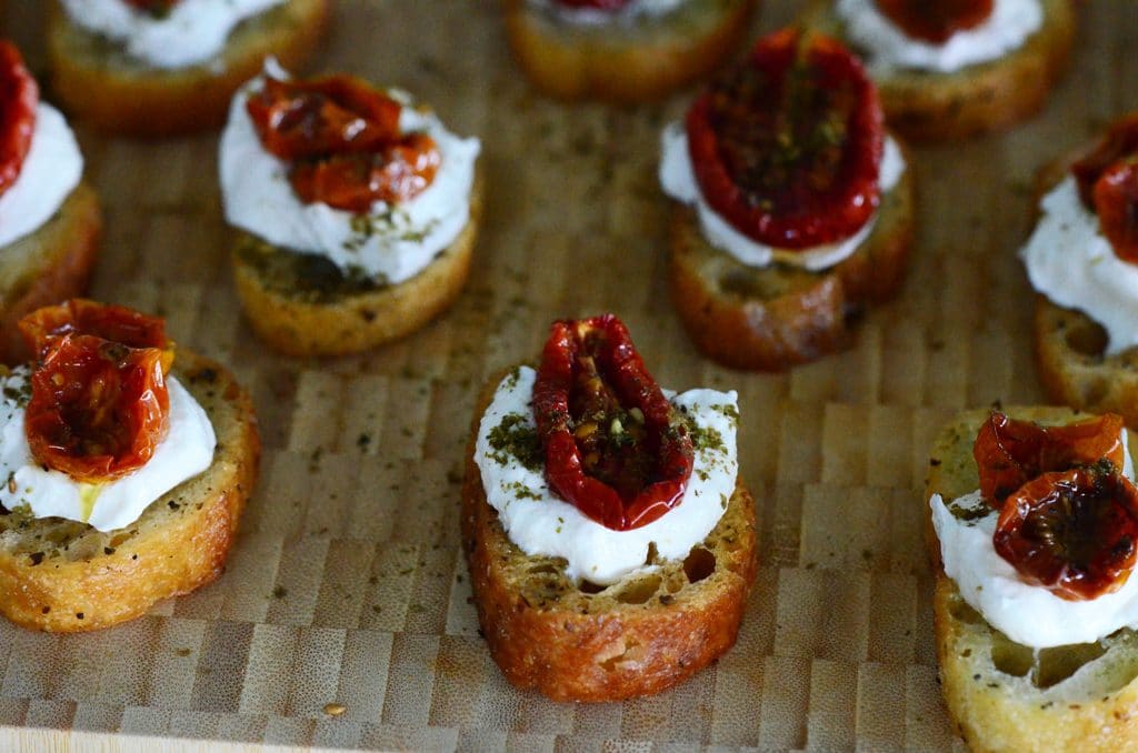 Za'atar roasted tomatos with labneh on crostini, displayed on a cutting board, Maureen Abood