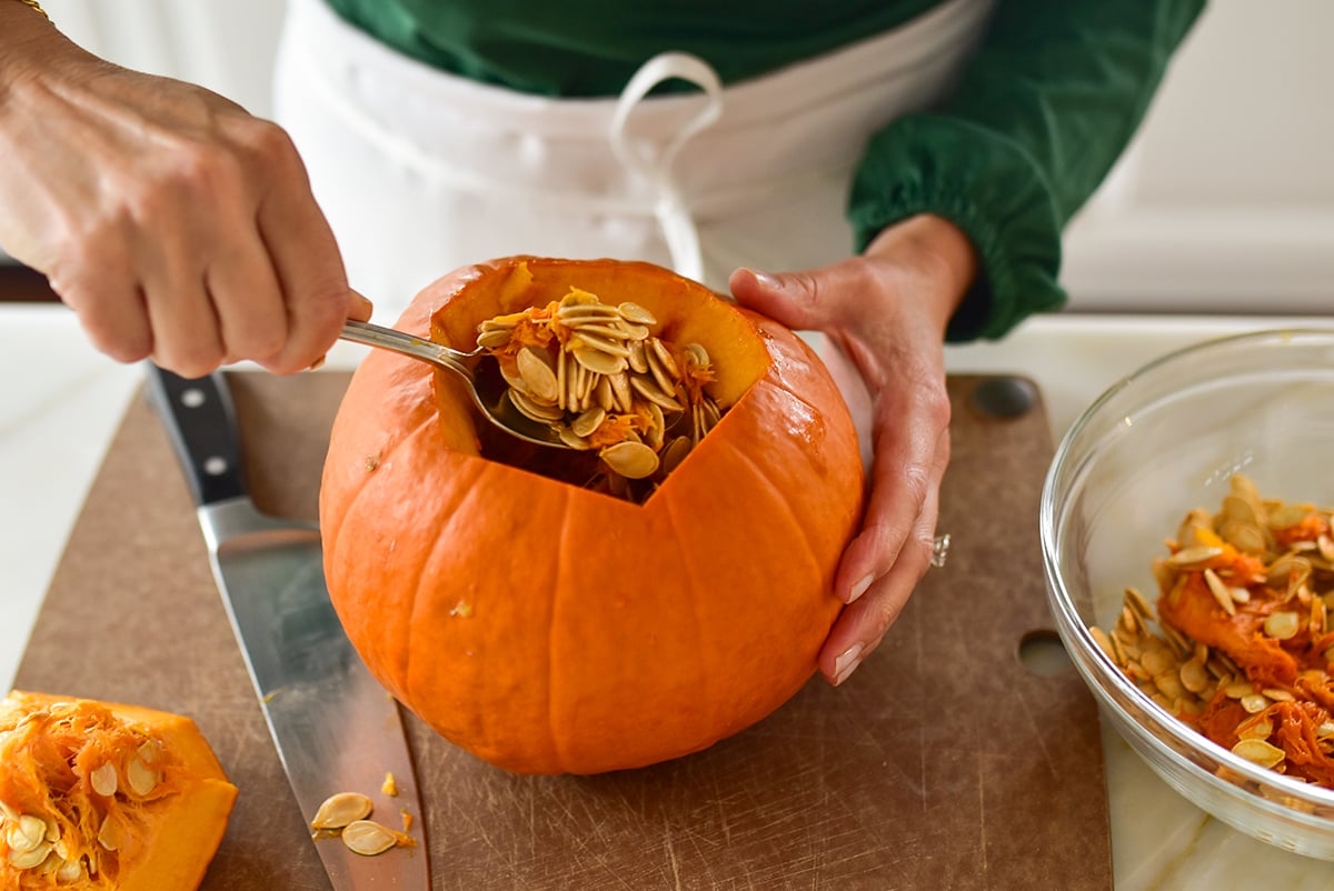 A hand scooping pumpkin seeds from a pumpkin