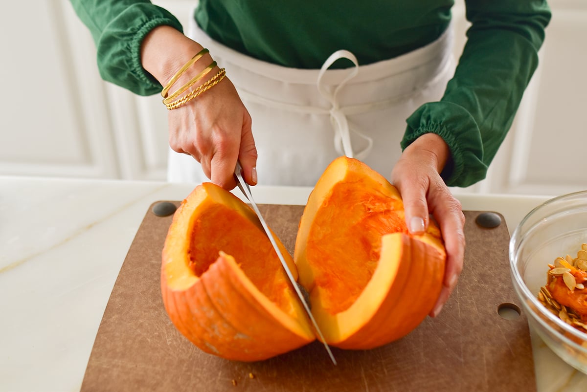 two hands slicing a pumpkin in half