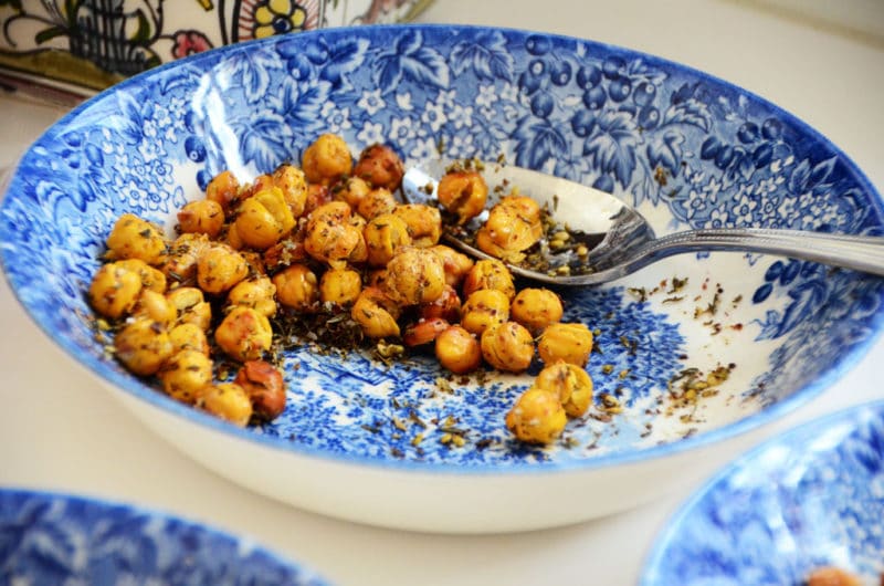 Roasted chickpeas in a blue bowl with a silver spoon.