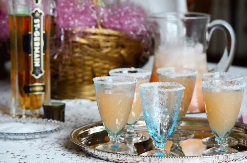 Glasses of grapefruit mimosas on a silver tray with a bottle of St. Germain in the background.