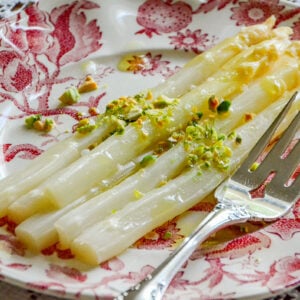 White asparagus on a pink plate with pistachios and a silver fork on the side